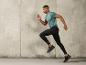 Homme en chemise grise et leggings noirs en train de courir.