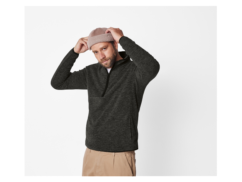 Homme en pull gris foncé et pantalon beige essayant un bonnet beige clair.