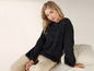 Une femme porte un pull noir moelleux et un pantalon beige.