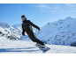 Homme snowboarder en combinaison noire et casque à la montagne, entouré de neige.