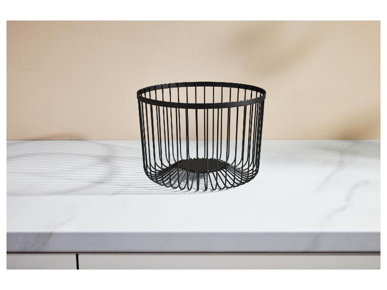 Corbeille à fruits en fil de fer noir sur un comptoir en marbre blanc avec un mur beige