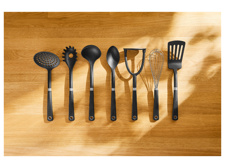 Sept ustensiles de cuisine noirs Zwilling J.A. Henckels disposés sur une surface en bois.