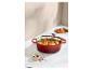 Cocotte ovale en fonte rouge avec poulet rôti et légumes, avec des épices à côté.