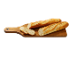 Deux baguettes, une entière et une tranchée, sur une planche à découper en bois.