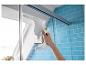 Nettoyeur de vitres à main nettoyant une paroi de douche dans une salle de bain aux carreaux bleus.