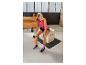 Femme en débardeur de sport rose et short noir assise sur une boîte d'entraînement, tenant une bouteille d'eau orange.