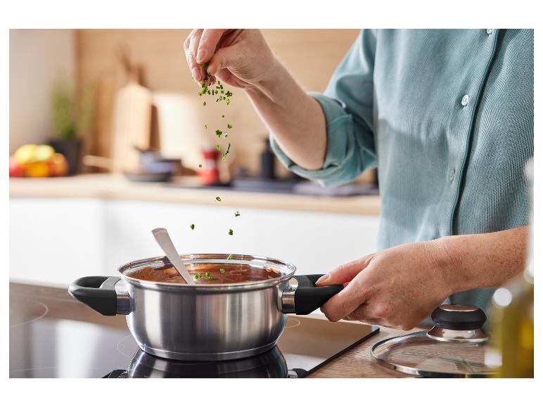 Une main ajoutant des herbes fraîches à une casserole sur une plaque à induction.