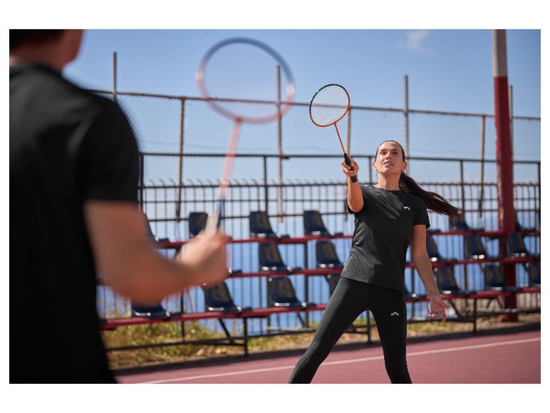 Femme et homme jouant au badminton sur un court extérieur, vêtus de tenues de sport noires.