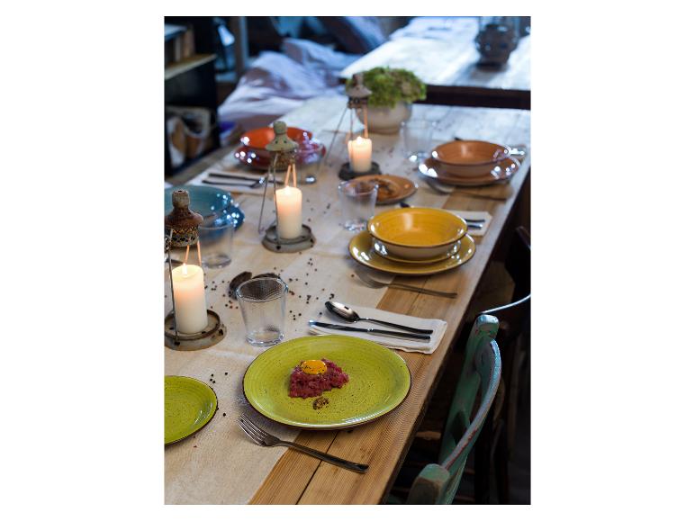 Table dressée avec des assiettes colorées, des bougies et un plat de tartare de bœuf.