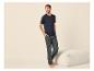 Homme en T-shirt bleu foncé et pantalon de pyjama foncé à motifs, debout près d'un pouf.
