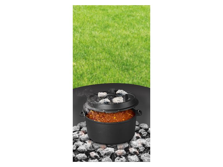 Marmite en fonte avec de la nourriture cuisant sur des charbons, sur fond d'herbe verte.