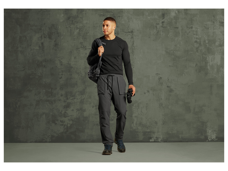 Un homme portant un pull noir et un pantalon gris avec un sac à dos et des jumelles.