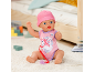 Poupée bébé en grenouillère et bonnet roses, avec sucette, assise sur un tapis.