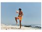 Homme en short de bain orange jouant avec un ballon de plage sur une plage de sable.