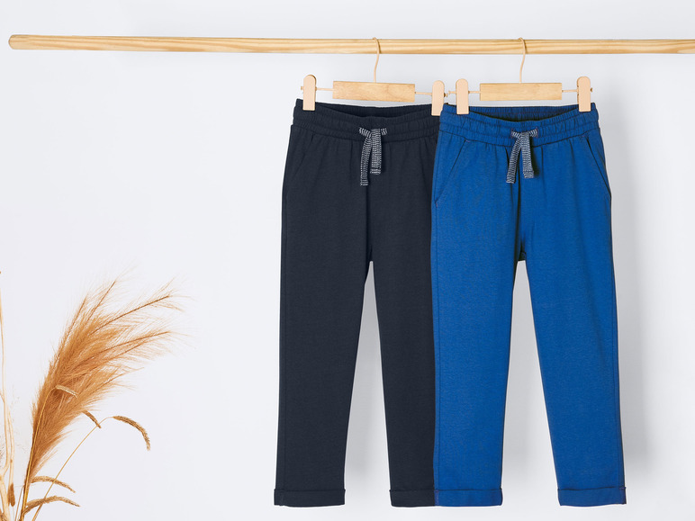 Deux pantalons de survêtement, l'un bleu et l'autre noir, suspendus à un cintre en bois.