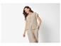 Femme en chemise beige à manches courtes et pantalon, riant sur fond blanc.