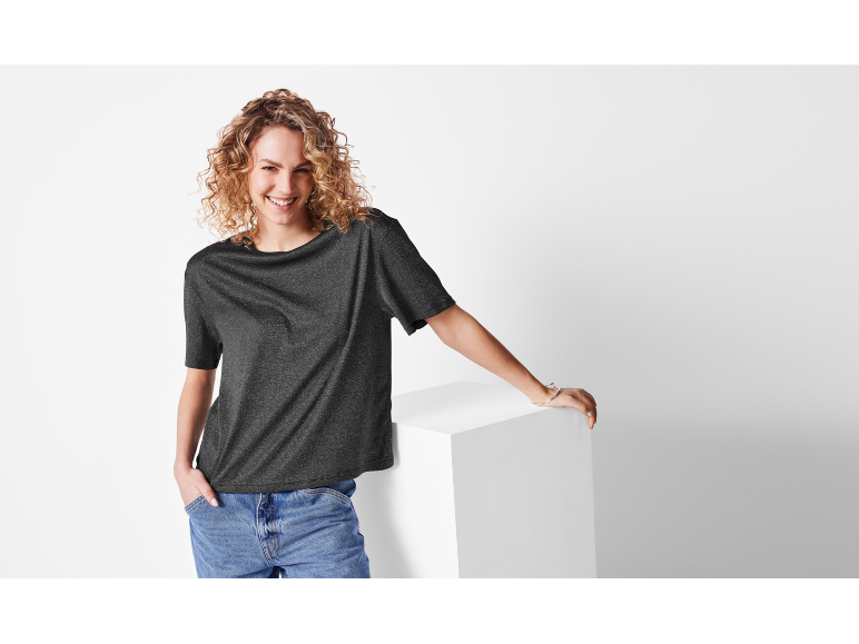 Une femme aux cheveux blonds porte un t-shirt gris foncé et un jean.