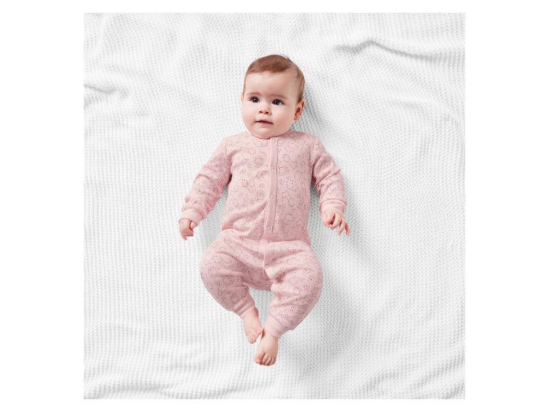 Bébé portant un pyjama rose à motifs animaux sur un plaid blanc.