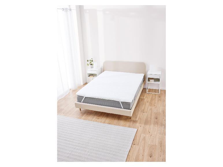 Protège-matelas blanc sur un lit dans un décor minimaliste.