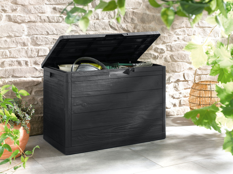 Une boîte de rangement noire à l'aspect bois, adaptée pour l'extérieur, ouverte avec des outils de jardin
