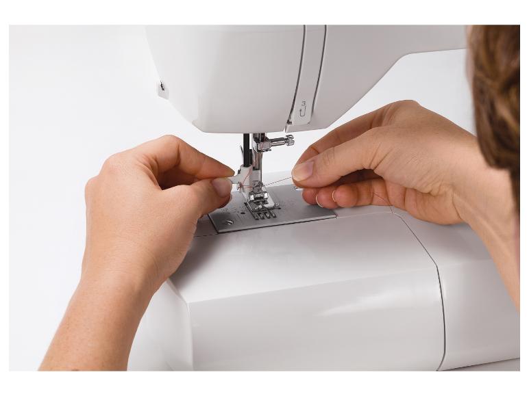 Gros plan de mains enfilant une machine à coudre avec du fil rouge.