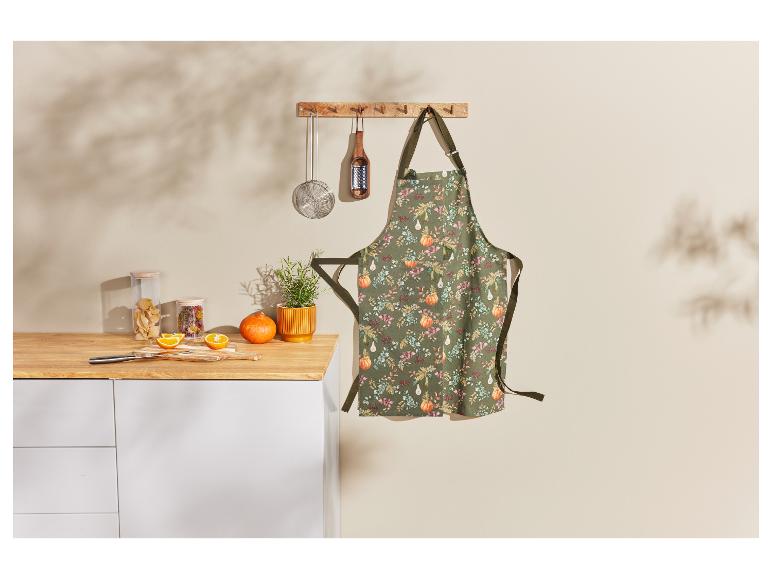 Tablier de cuisine à motif d'automne avec des citrouilles et des feuilles, accroché à un crochet.
