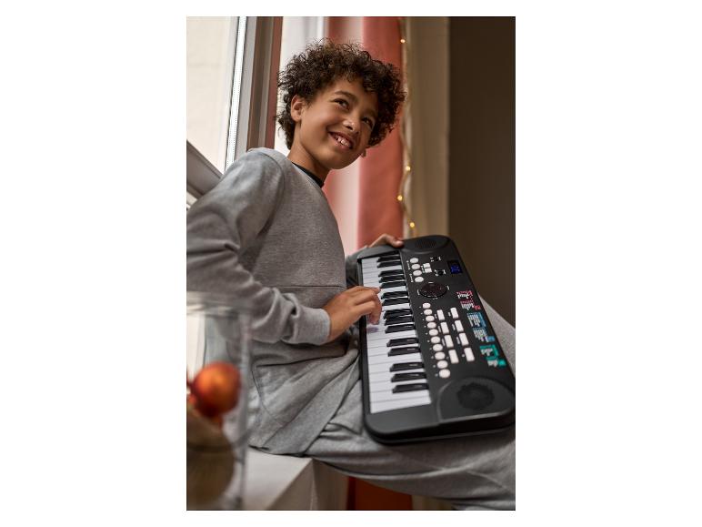 Garçon assis près de la fenêtre jouant d'un piano électronique noir.