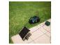 Robot tondeuse vert avec station de charge et panneau solaire dans un jardin.
