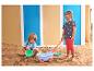 Deux enfants jouent dans un bac à sable avec des jouets de plage, dont un chariot et des seaux.
