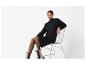 Femme en robe pull noire, collants et bottines, assise sur une chaise en métal.