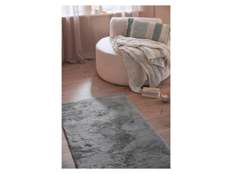 Un tapis en fourrure grise devant un fauteuil blanc avec une couverture et un coussin.