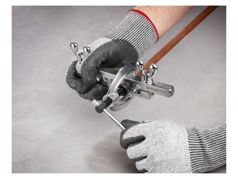 Des mains gantées utilisent un outil Parkside pour cintrer des tuyaux en cuivre.