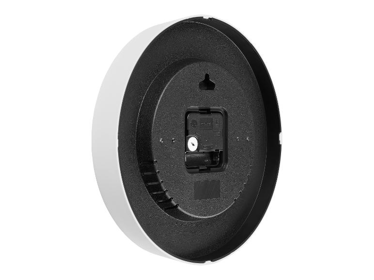 Arrière d'une horloge murale noire et blanche avec mécanisme à quartz et compartiment à piles.