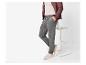 Homme en pantalon de jogging gris, t-shirt beige et veste marron, appuyé sur un tabouret.