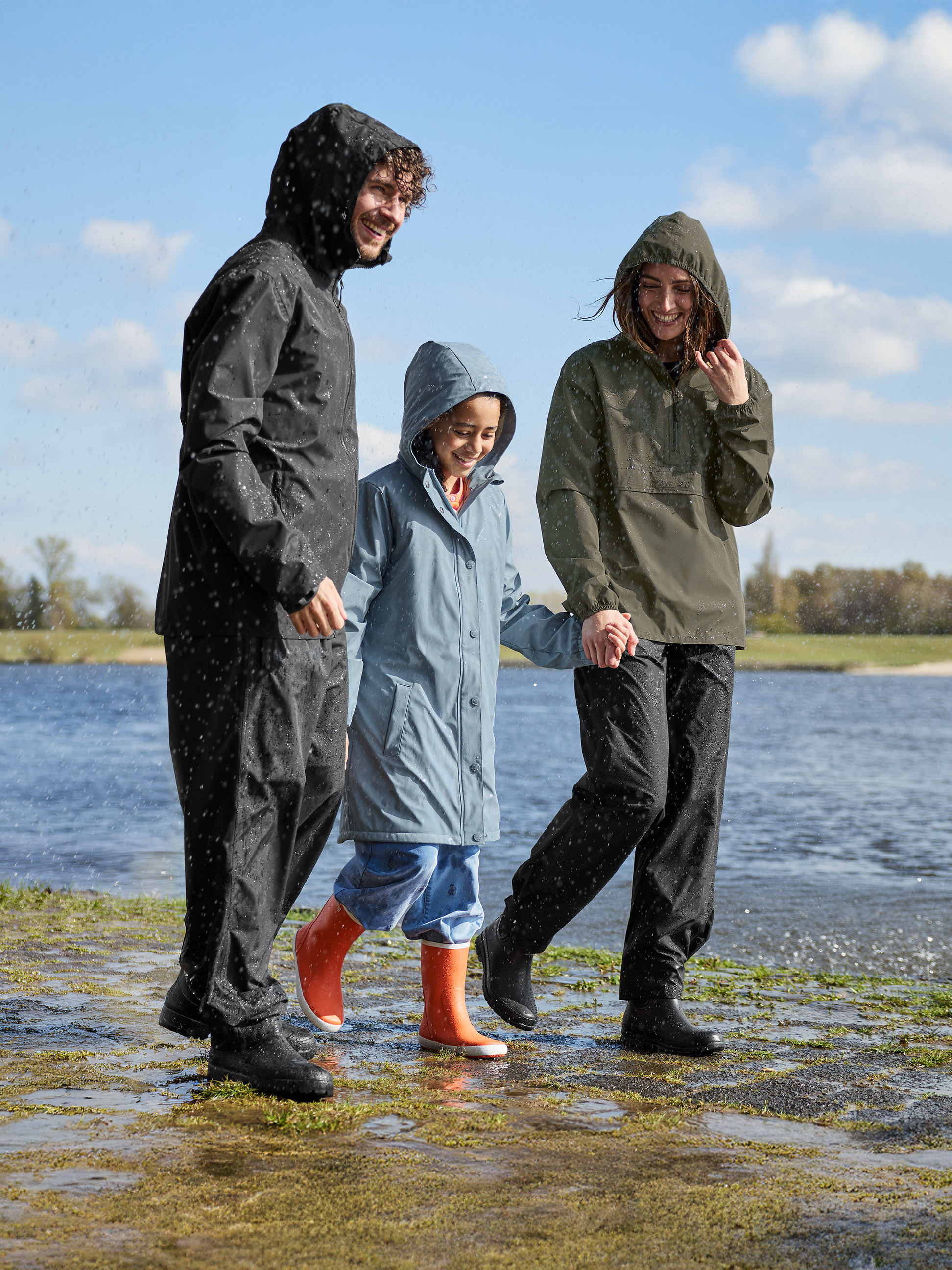 Famille souriante en imperméables et bottes de pluie, marchant près de l'eau.