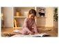 Fille souriante en pyjama rose coloriant un livre sur un tapis avec des crayons.