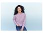 Une femme en pull rose et en jean sourit à la caméra.