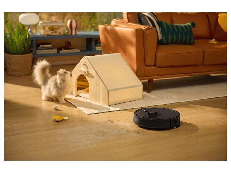 Robot aspirateur nettoyant les poils de chat sur un parquet, avec un chat et une niche en bois.
