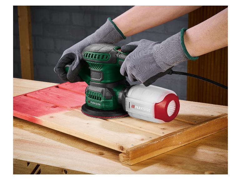 Personne utilisant une ponceuse orbitale aléatoire Parkside sur une surface en bois, partiellement peinte en rouge.
