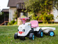 Un tracteur jouet blanc avec un siège rose et des roues bleues dans l'herbe.