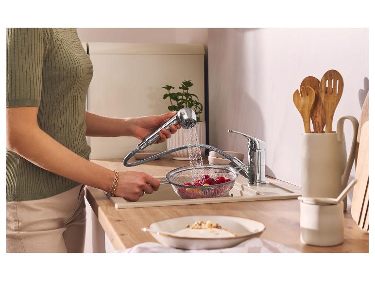 Femme lavant des baies dans une passoire avec un robinet extractible dans une cuisine moderne.