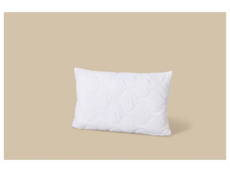 Oreiller blanc matelassé avec un motif ondulé sur fond beige.