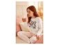 Femme en pyjama blanc avec un imprimé Minnie Mouse, assise sur un lit avec une tasse