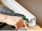 Personne utilisant une perceuse avec un adaptateur d'angle pour visser dans une goulotte blanche.
