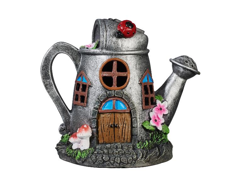 Un arrosoir en métal transformé en maison de conte de fées avec une porte, des fenêtres, des fleurs et des champignons.