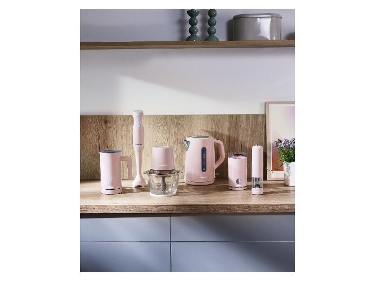 Appareils de cuisine roses: bouilloire, mixeur plongeant, hachoir, mousseur à lait et moulin à épices sur un comptoir en bois.