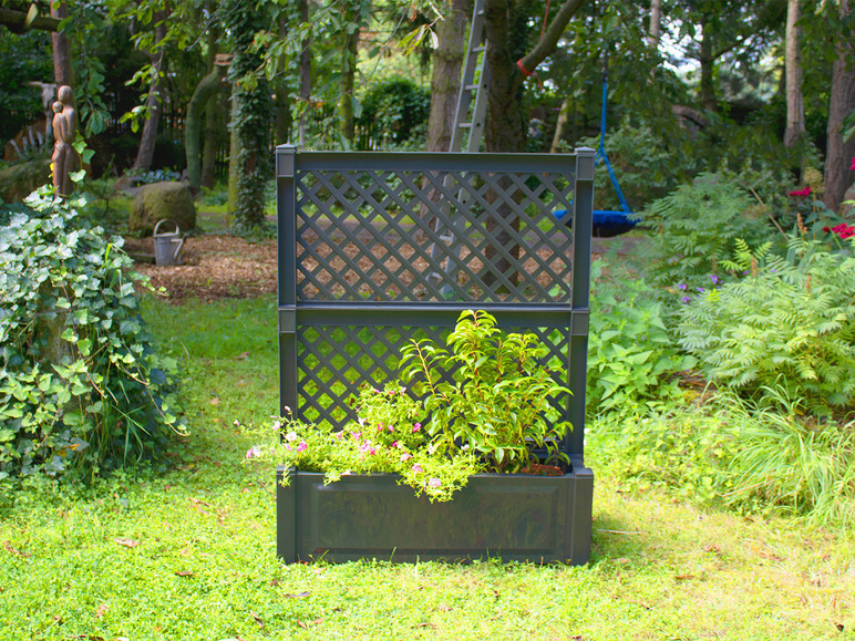 Une jardinière noire avec un treillis dans un jardin vert.