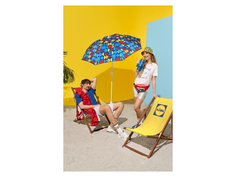 Homme et femme à la plage avec parasol, transat, sac banane et tasse aux motifs géométriques.