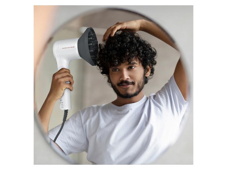 Homme se séchant les cheveux bouclés avec un sèche-cheveux blanc et diffuseur dans un miroir.