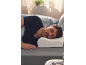 Homme dormant sur le côté sur une literie grise, la tête sur un oreiller ergonomique.